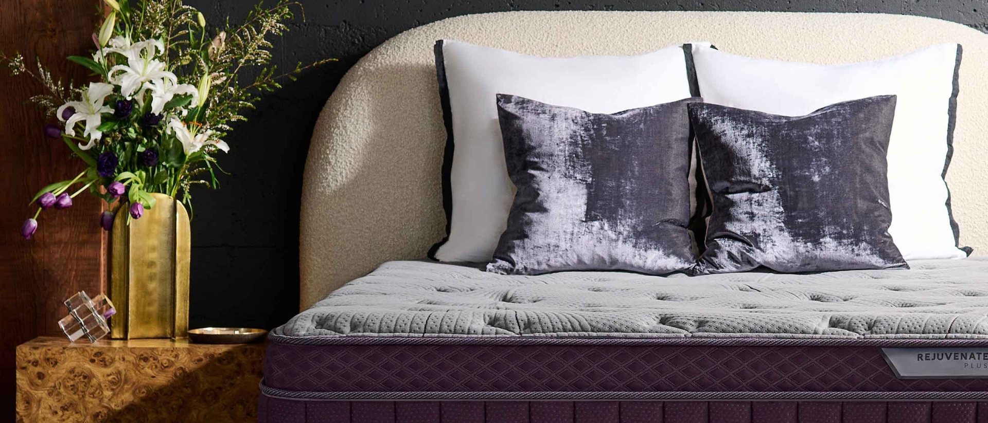 Purple RejuvenatePlus™ Mattress on a sherpa bed frame next to a nightstand with a large bouquet.