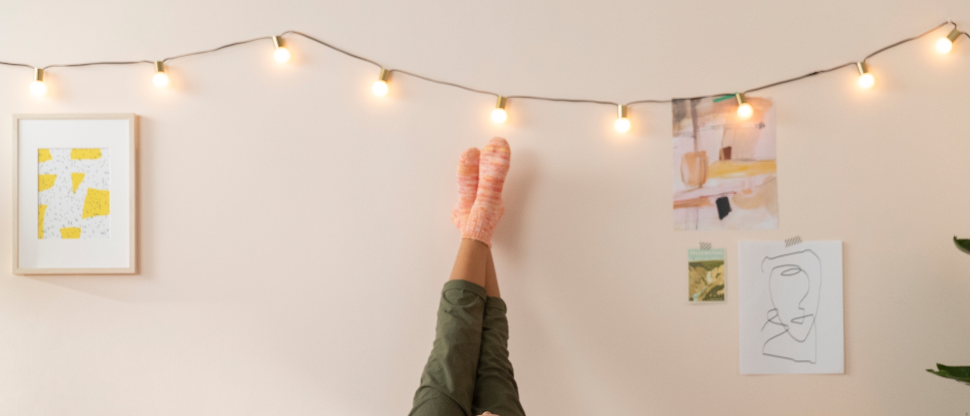 A girl wearing purple headphones lies on a full size bed on her back with her legs up the wall in a teen bedroom.